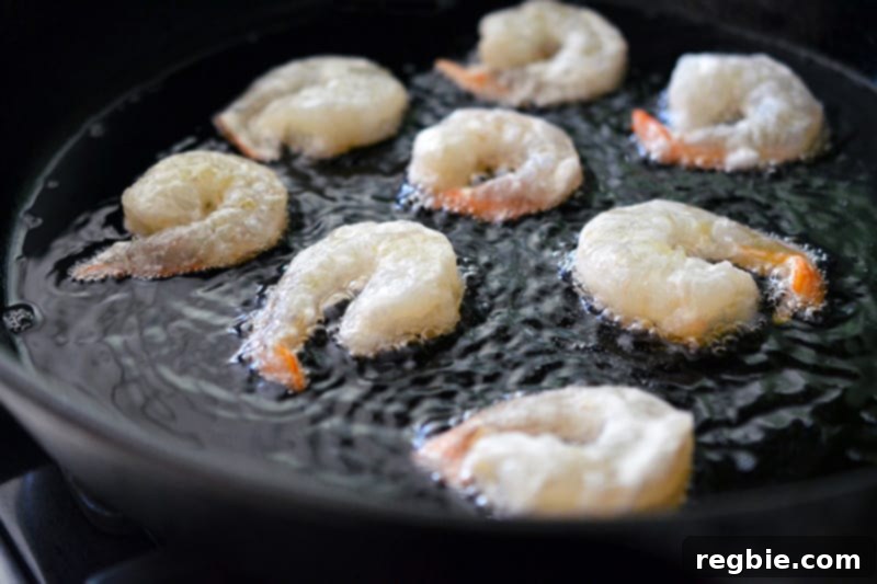 Frying the battered shrimp in a cast iron skillet, achieving a golden crust for Paleo Walnut Shrimp.