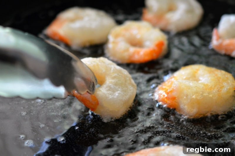 Using tongs to flip golden brown Paleo Walnut Shrimp, showcasing their perfectly fried exterior.