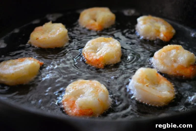 Paleo Walnut Shrimp frying in a cast iron skillet until they are golden and opaque.