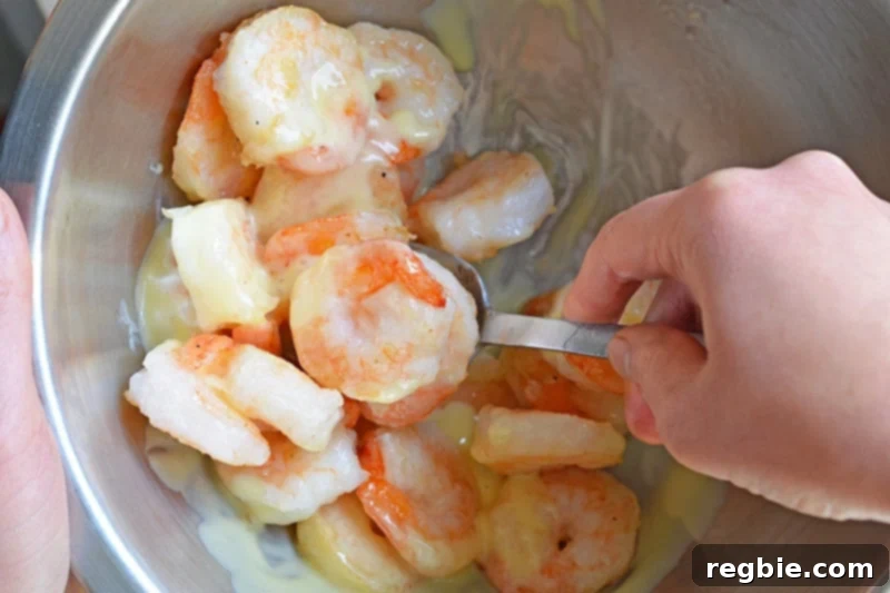 Tossing the Paleo Walnut Shrimp in the creamy dressing within a silver bowl, ensuring every piece is coated.