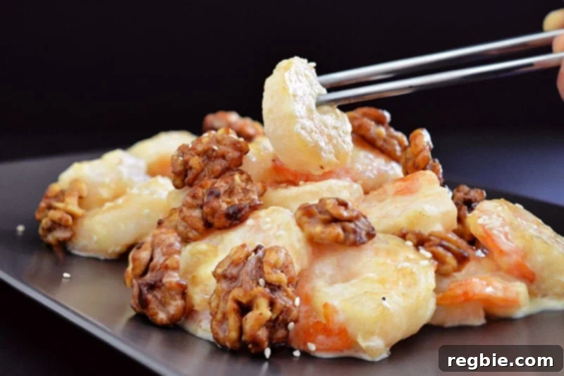 A side view of metal chopsticks delicately picking up a piece of golden-brown Paleo Walnut Shrimp, coated in a creamy sauce.