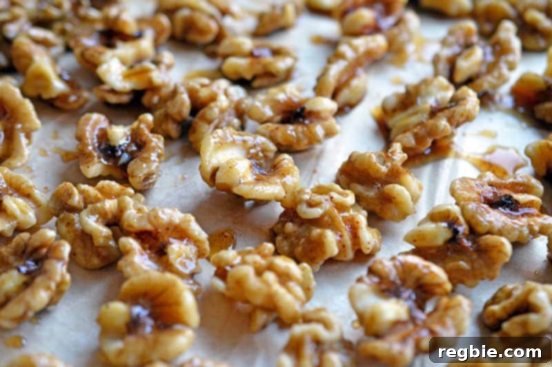 Maple spiced walnuts spread thinly and evenly on a piece of parchment paper on a baking sheet.