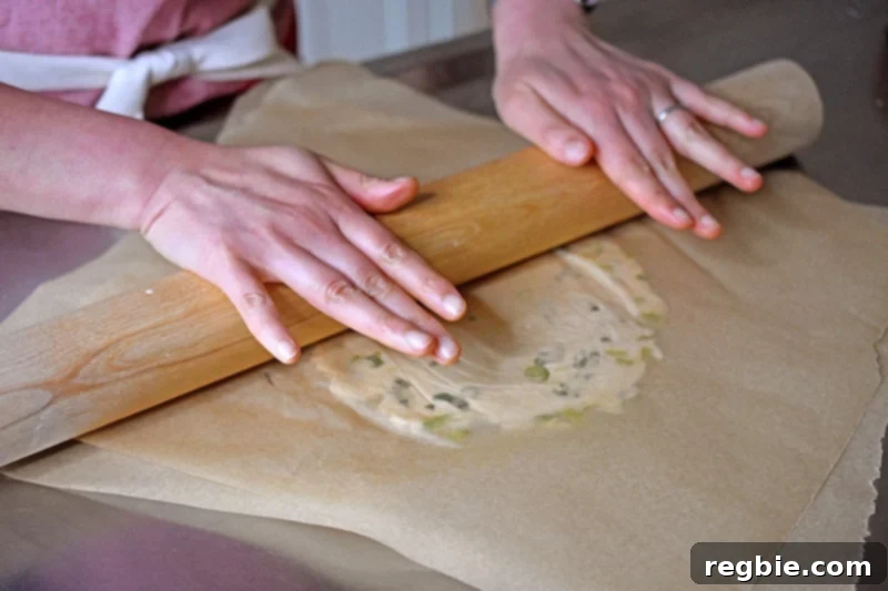 A shot of someone rolling out the Paleo Scallion pancake dough between parchment paper with a rolling pin.