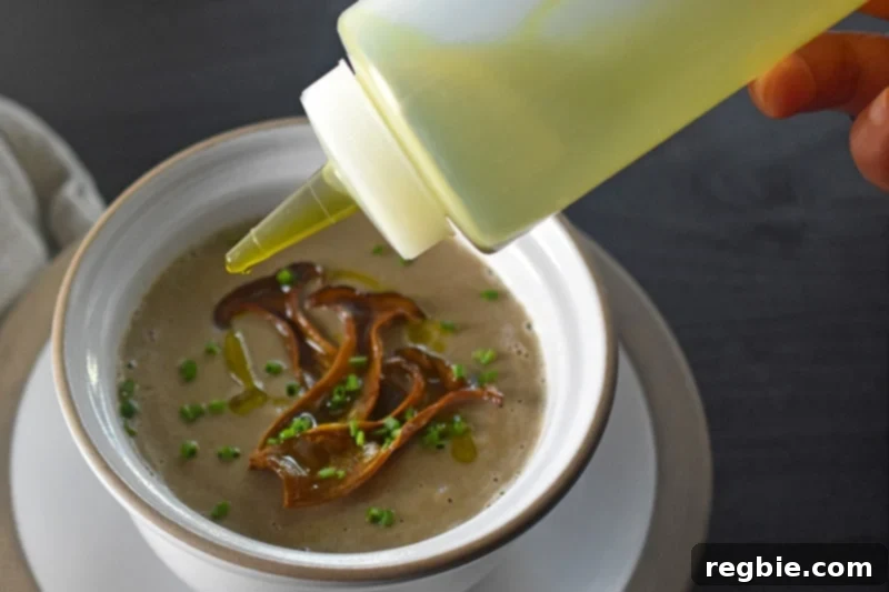 Someone garnishing the cream of mushroom soup with olive oil.
