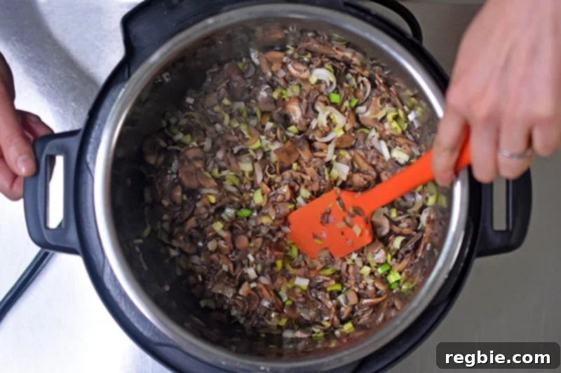 Someone mixing the mushrooms, leeks, and shallots in an Instant pot for Instant Pot cream of mushroom soup.
