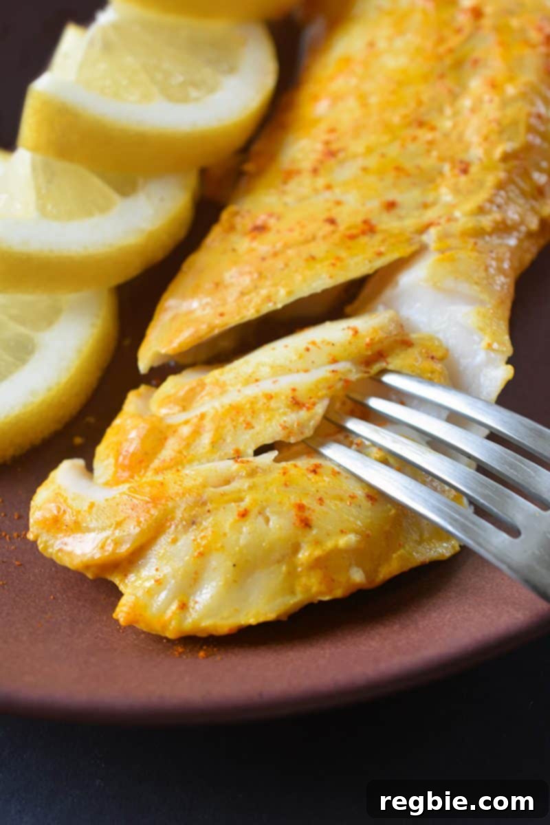 A closeup of perfectly cooked Tandoori Fish on a plate with sliced lemons, highlighting the golden-brown crust and juicy interior.