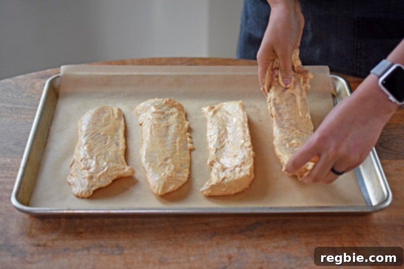 Four pieces of Tandoori Fish are carefully placed on a parchment-lined rimmed baking sheet, ready for the oven.