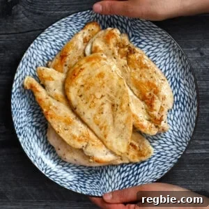 How I Cook Juicy, Tender Chicken Breasts Every Time 13 Two hands are holding a blue plate filled with golden brown, perfectly cooked boneless, skinless chicken breasts.