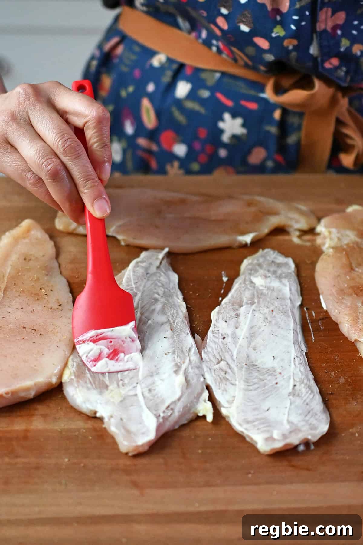 How I Cook Juicy, Tender Chicken Breasts Every Time 8 Brushing on a thin layer of mayonnaise on thinly cut raw boneless skinless chicken breasts with a small red spatula.